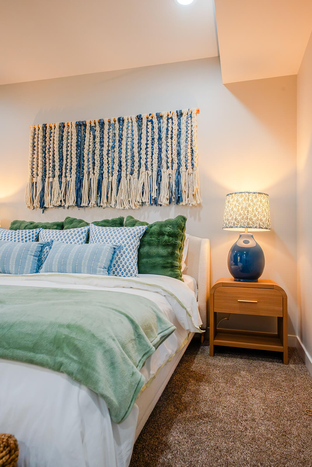 Okoboji-Lake-House-33 Bright bedroom featuring woven blue wall art, layered neutral bedding, and sophisticated coastal interior design
