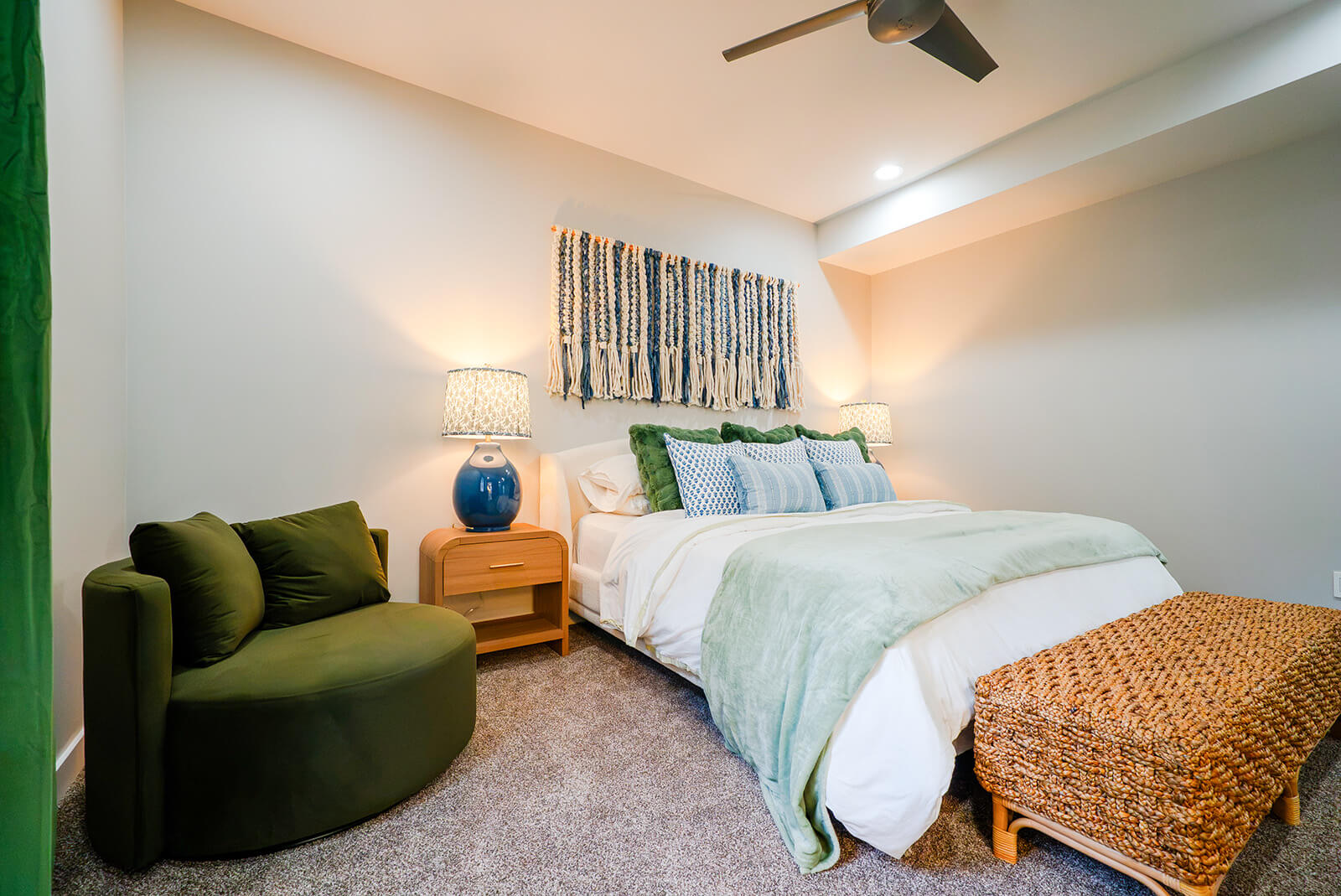 Okoboji-Lake-House-36 Bright lake house bedroom with woven wall art, soft blue accents, layered bedding, and chic coastal-inspired design