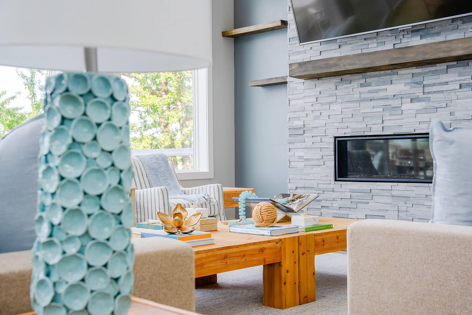 Okoboji-Lake-House-4 Cozy living room with stone fireplace, framed TV, light blue accents, and layered neutral furnishings