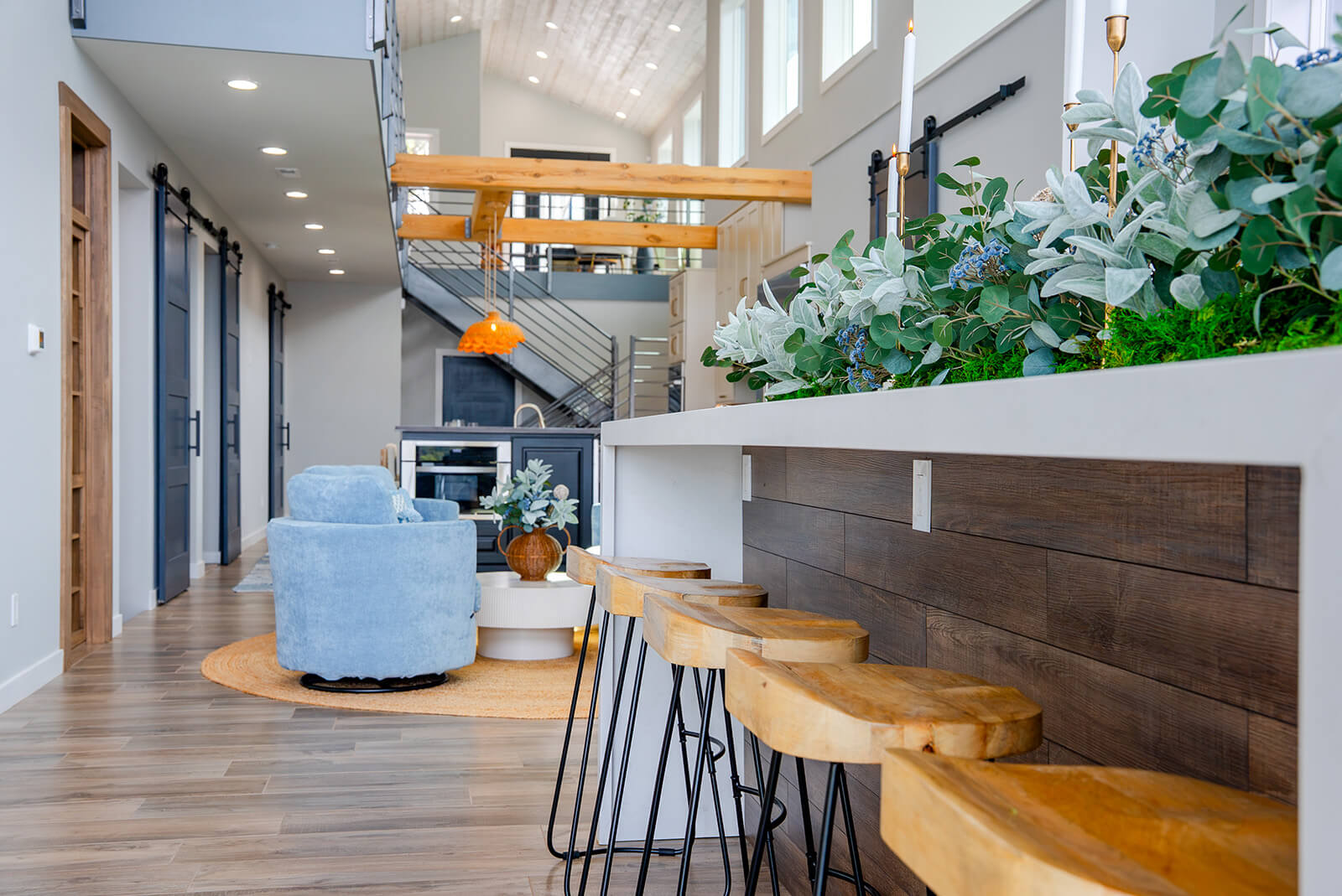 Okoboji-Lake-House-9 Open living space with natural wood beams, sculptural lighting, and lush greenery