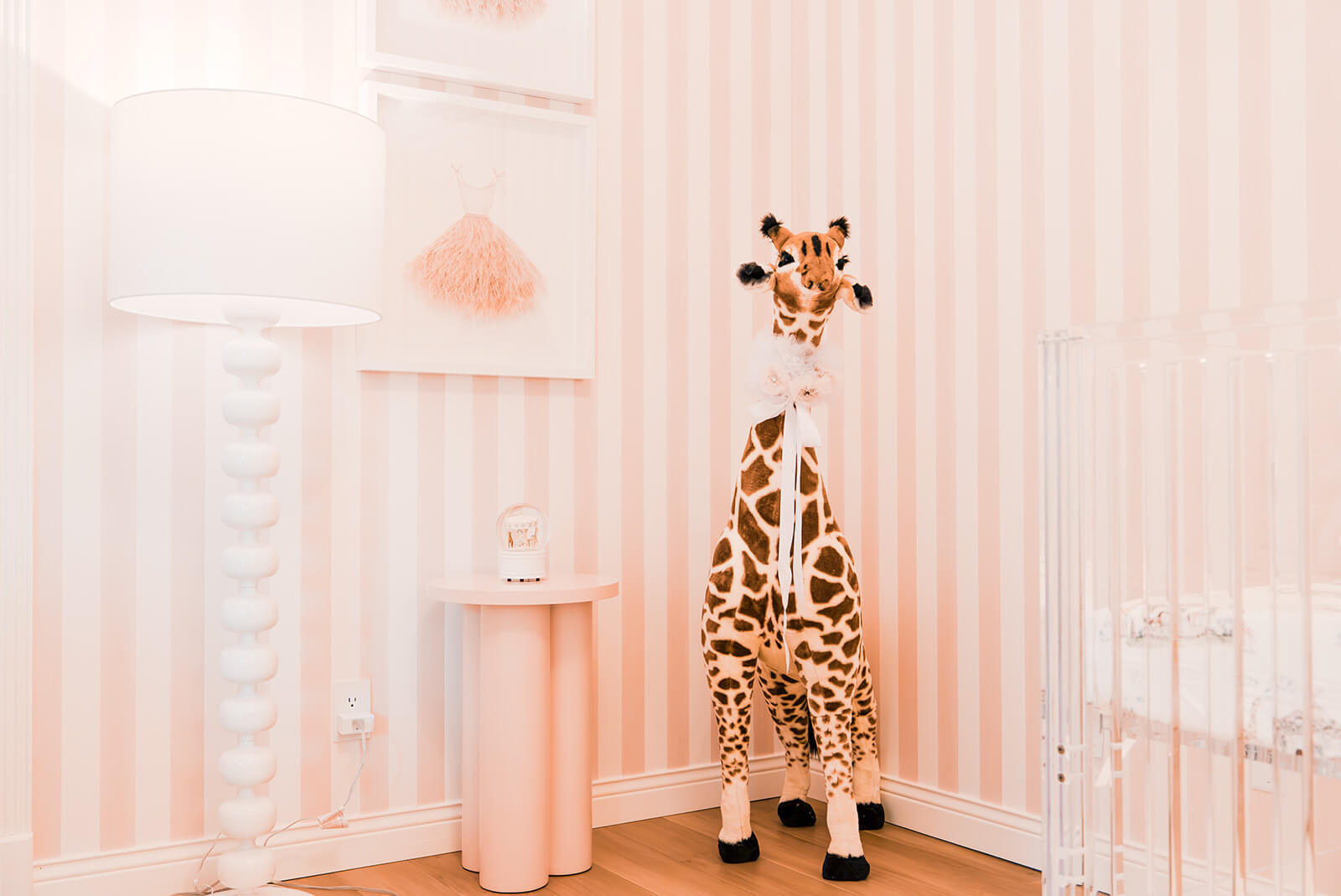 Storybook-11 Playful nursery corner featuring a giraffe sculpture, white furnishings, and soft pink striped walls