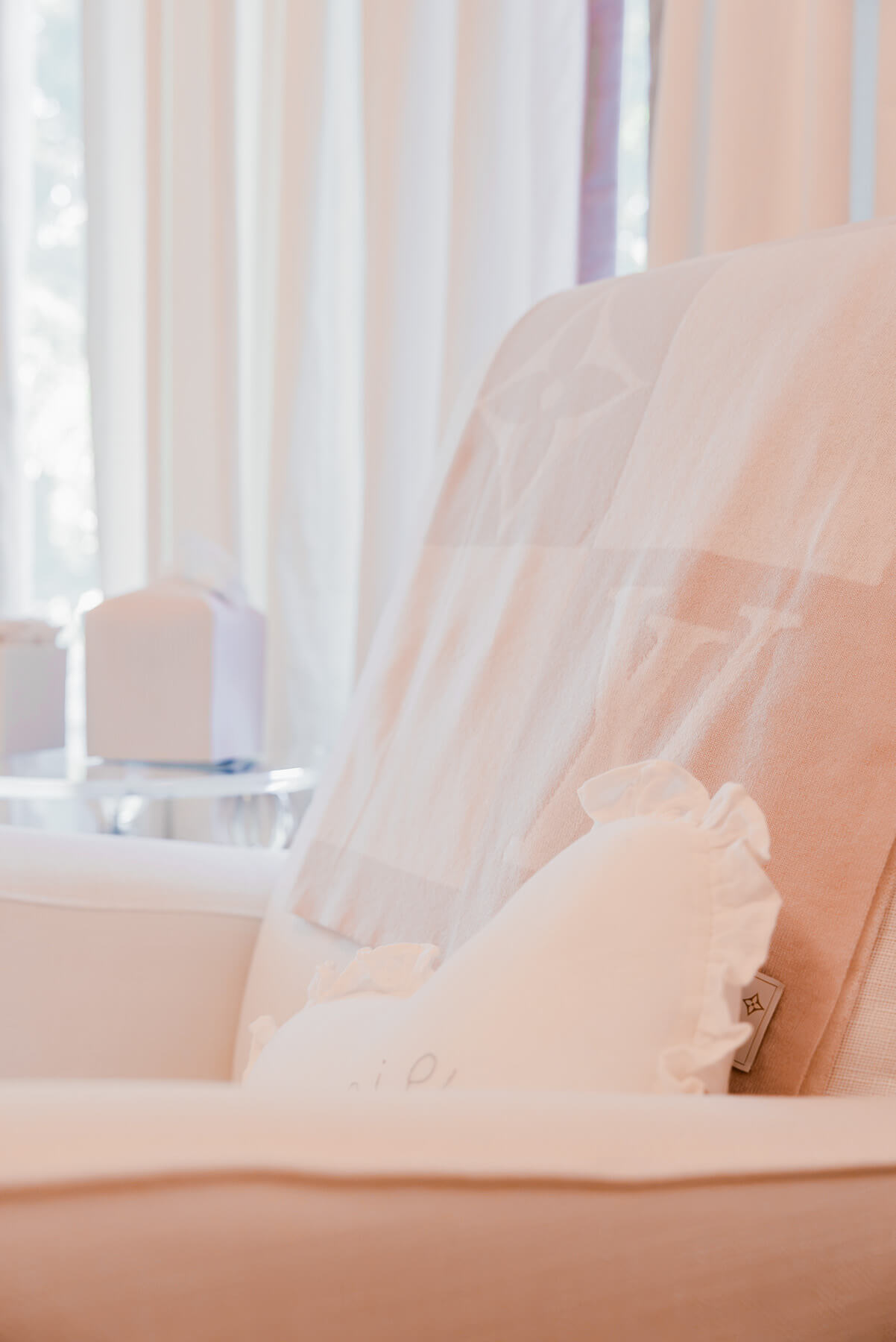Storybook-12 Serene nursery with a white upholstered chair, soft pink accents, sheer curtains, and abundant natural light
