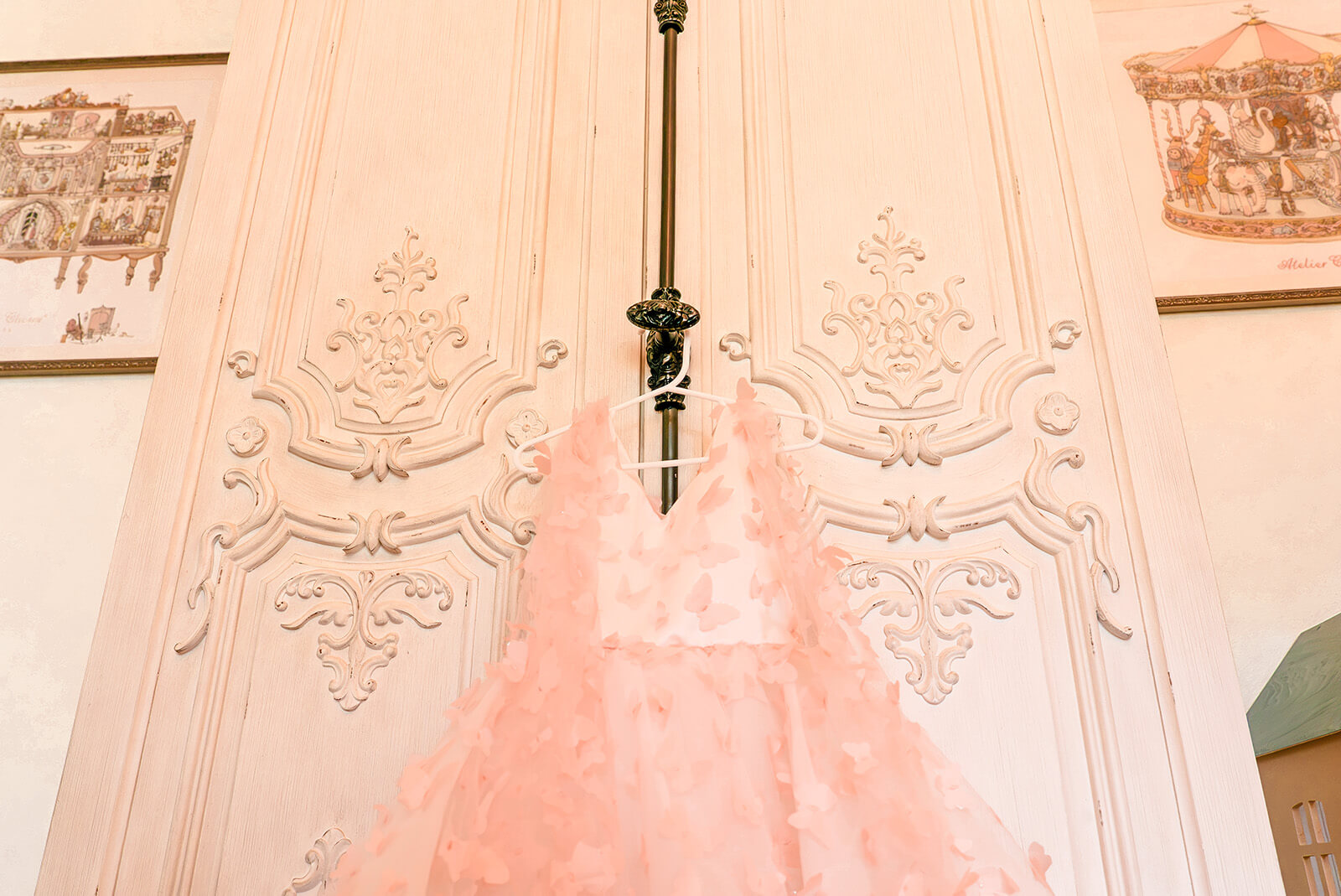 Storybook-35 Ornate white wardrobe doors with delicate detailing and a soft pink garment hanging at the center