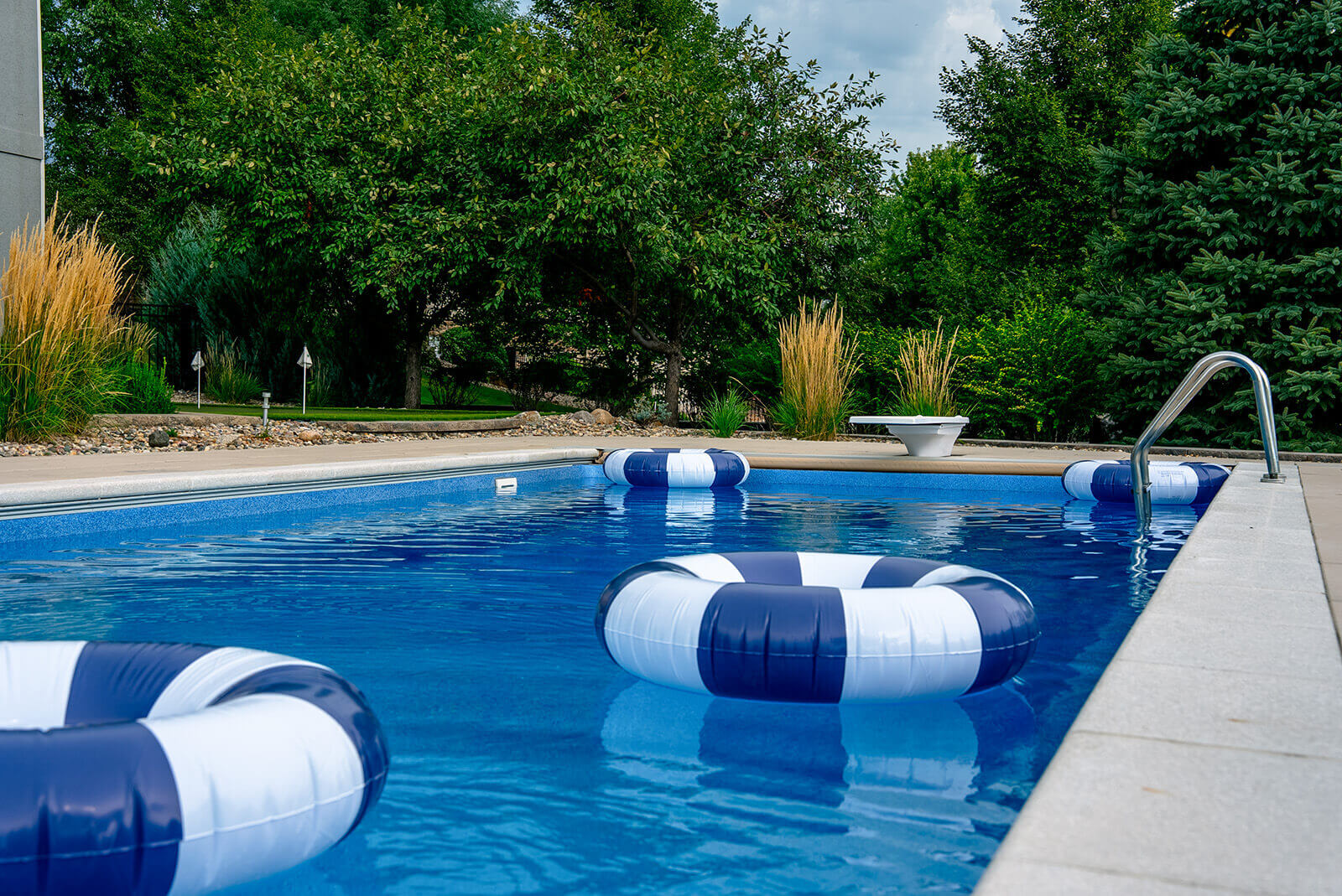 taylor-jane-project-33 Blue swimming pool with floating loungers surrounded by mature trees and lush green landscaping