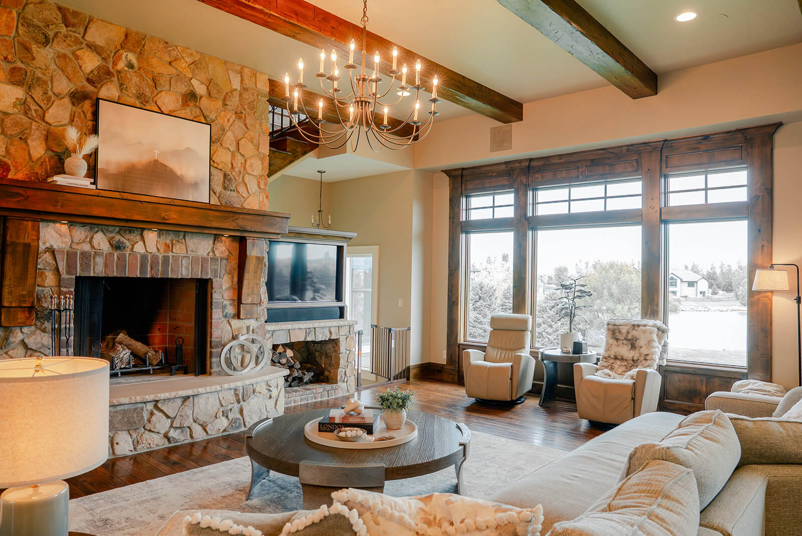 the-hearth-project-1 Elevated living room with stone fireplace, exposed wood beams, and warm layered furnishings