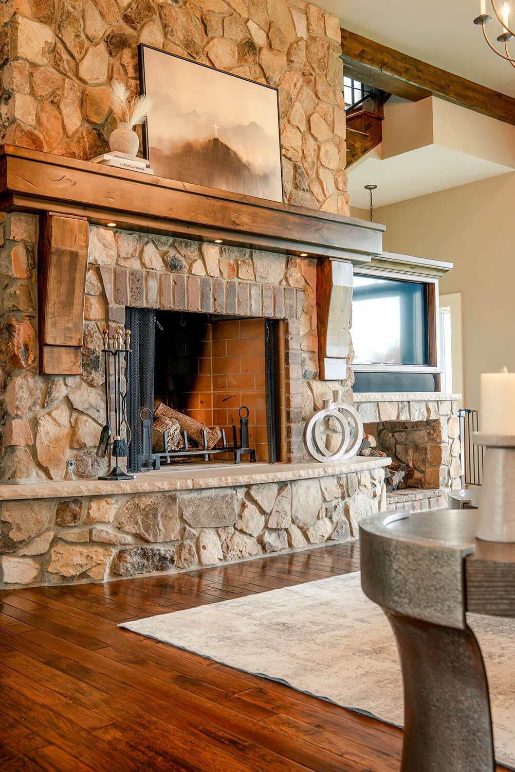 the-hearth-project-3 Refined living room with stone fireplace, leather chair, wood beams, and warm natural textures
