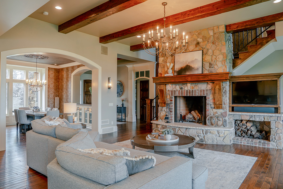 hearth-project-add-6 Open-concept living room with stone fireplace, exposed beams, and neutral furnishings