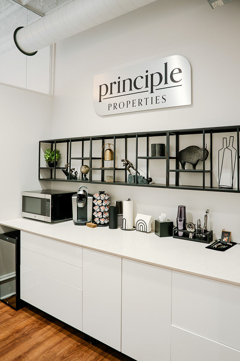 principle-properties-project-1 White built-in cabinetry and shelving in a modern office with a framed Principle Properties sign