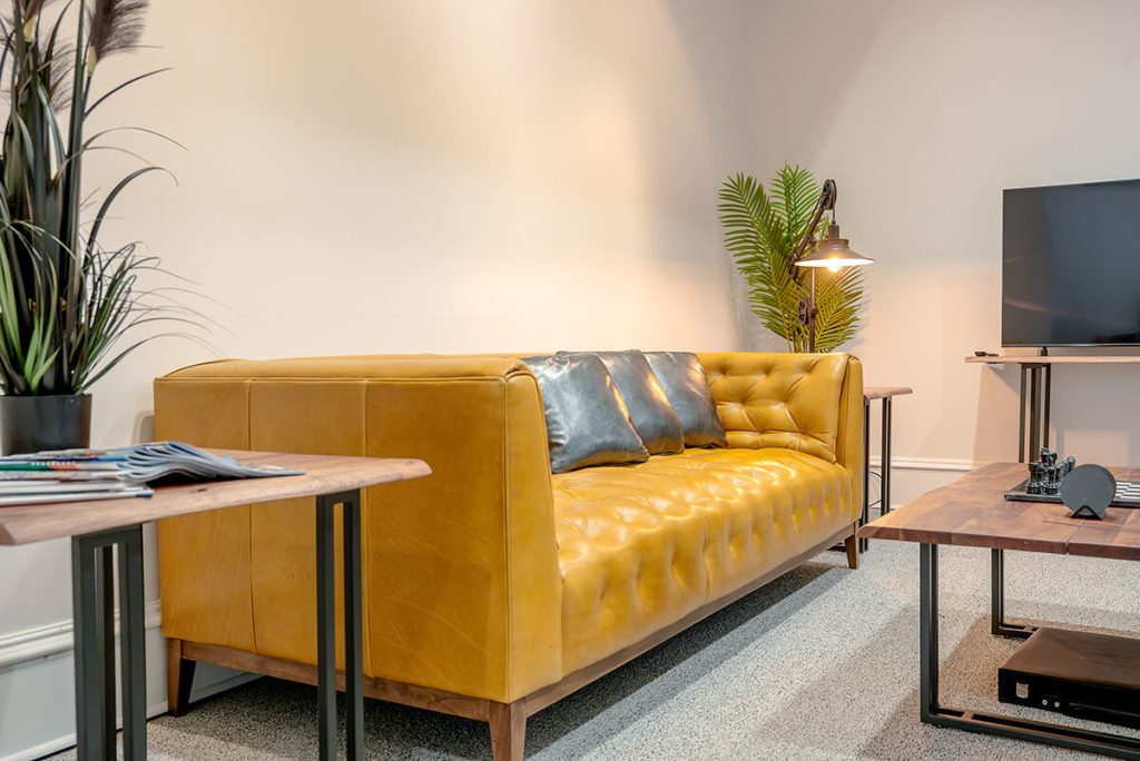 principle-properties-project-9 Mustard yellow leather sofa and wood side table in a modern office lounge
