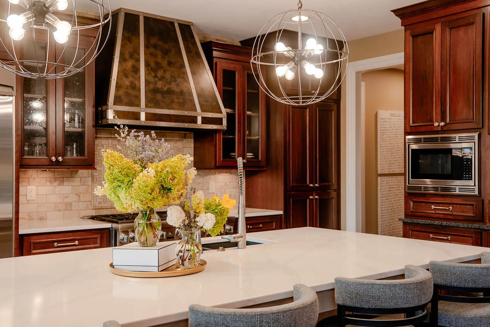 taylor-jane-project-45 Warm kitchen with rich wood cabinetry, stone surfaces, and statement pendant lighting
